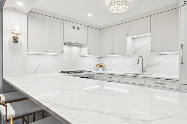 kitchen featuring a sink, light stone countertops, white cabinetry, backsplash, and recessed lighting