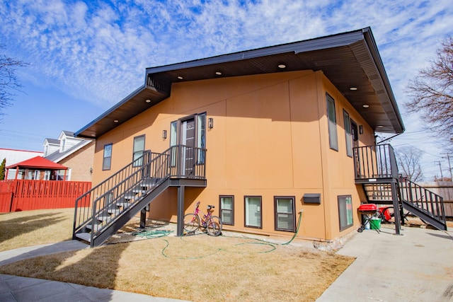 back of house featuring stairs, fence, and stucco siding