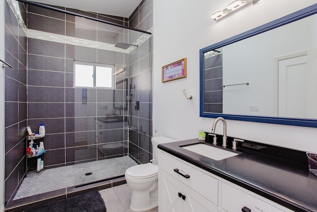 bathroom featuring tile patterned flooring, a tile shower, vanity, and toilet