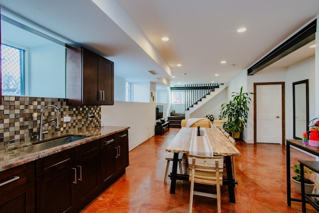 kitchen with light stone counters, recessed lighting, decorative backsplash, a sink, and dark brown cabinets