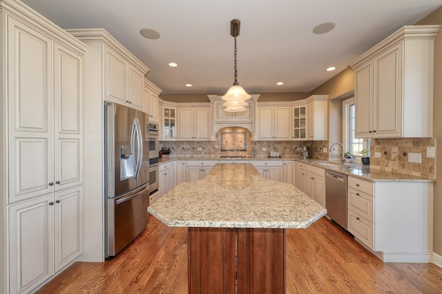 kitchen featuring light wood finished floors, a center island, glass insert cabinets, stainless steel appliances, and a sink