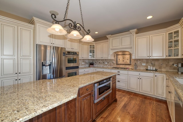 kitchen featuring backsplash, wood finished floors, appliances with stainless steel finishes, glass insert cabinets, and light stone countertops