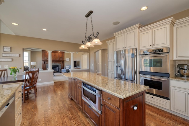 kitchen with a fireplace, arched walkways, cream cabinetry, appliances with stainless steel finishes, and light wood-type flooring