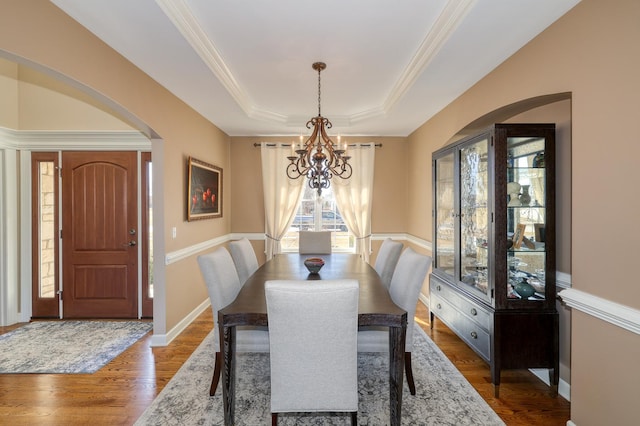 dining area featuring dark wood-type flooring, baseboards, a chandelier, a tray ceiling, and arched walkways