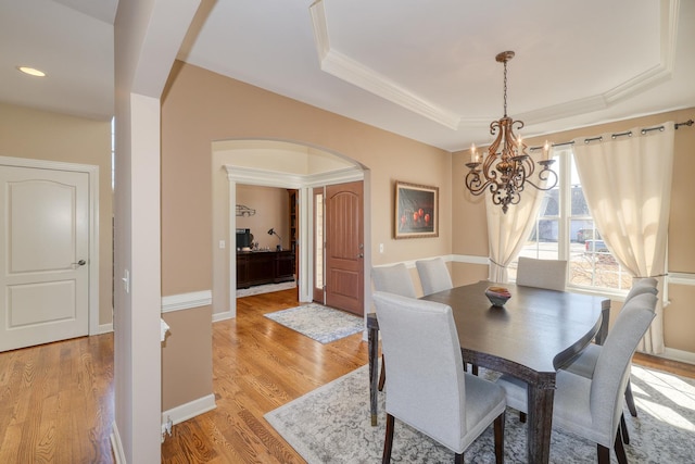 dining space featuring baseboards, a tray ceiling, arched walkways, light wood-type flooring, and a chandelier