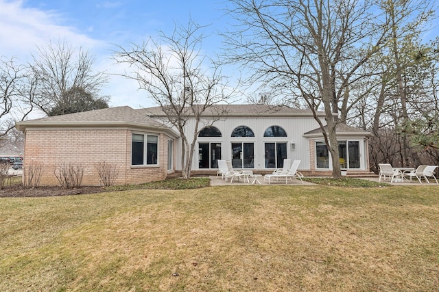 rear view of property with entry steps, a patio area, a lawn, and brick siding