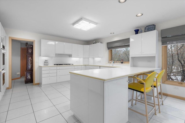 kitchen with a peninsula, white cabinetry, light countertops, a kitchen bar, and cooktop