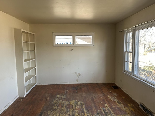 empty room with hardwood / wood-style floors, visible vents, and baseboards