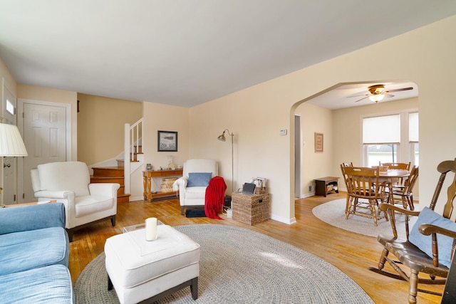 living room featuring arched walkways, stairway, light wood-style flooring, and baseboards