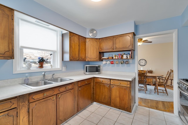 kitchen with light tile patterned floors, brown cabinetry, stainless steel appliances, light countertops, and a sink