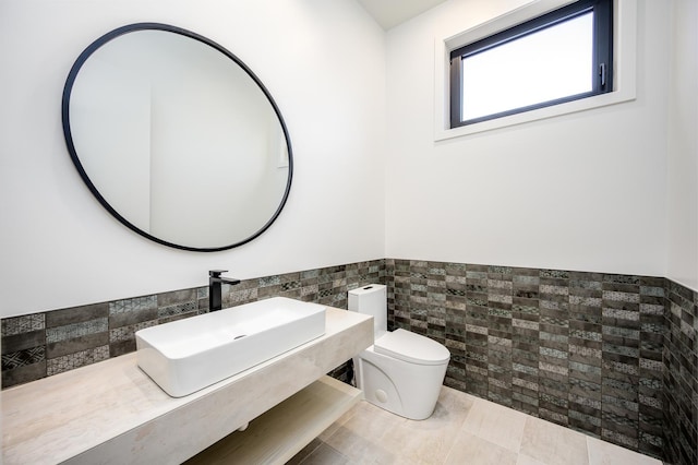 half bath featuring tile patterned floors, toilet, a sink, tile walls, and wainscoting