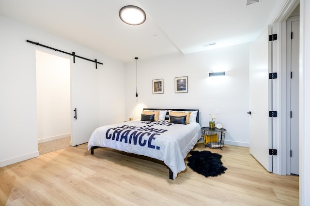 bedroom featuring a barn door, wood finished floors, visible vents, and baseboards