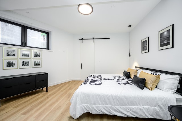 bedroom featuring baseboards, light wood-type flooring, and a barn door