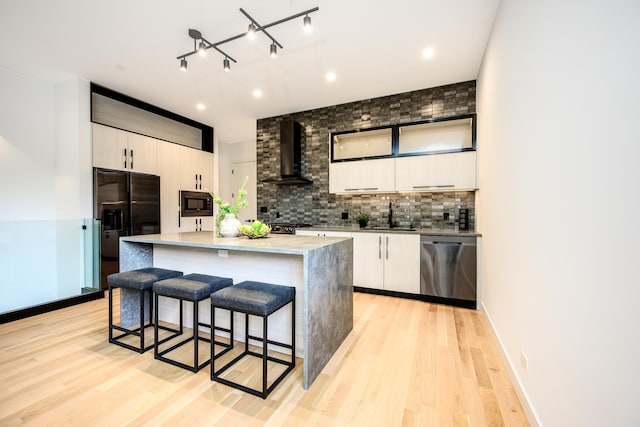 kitchen with black appliances, a kitchen breakfast bar, tasteful backsplash, light wood-style floors, and wall chimney range hood