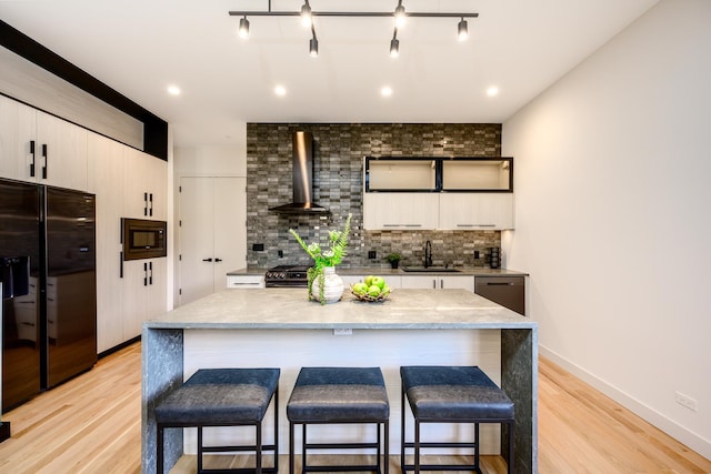 kitchen with tasteful backsplash, a kitchen bar, black appliances, wall chimney exhaust hood, and a sink