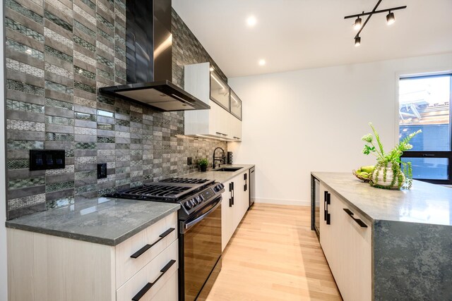 kitchen featuring light wood-style flooring, a sink, tasteful backsplash, black gas stove, and wall chimney range hood