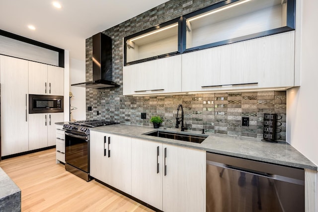 kitchen featuring built in microwave, a sink, black gas range, dishwasher, and wall chimney range hood