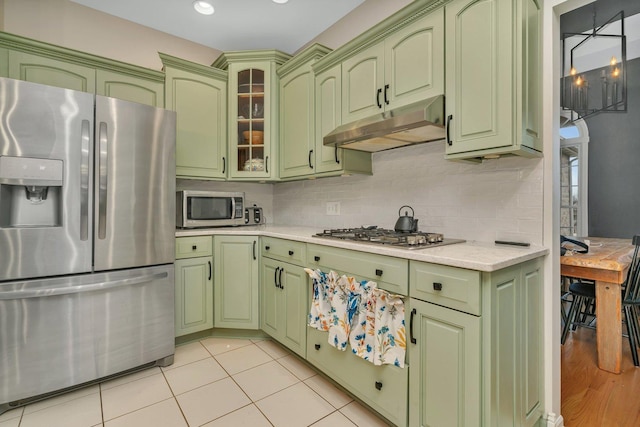 kitchen featuring under cabinet range hood, stainless steel appliances, green cabinets, light countertops, and tasteful backsplash