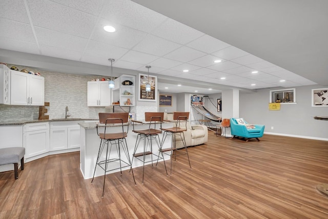 living area featuring a paneled ceiling, baseboards, wood finished floors, and recessed lighting