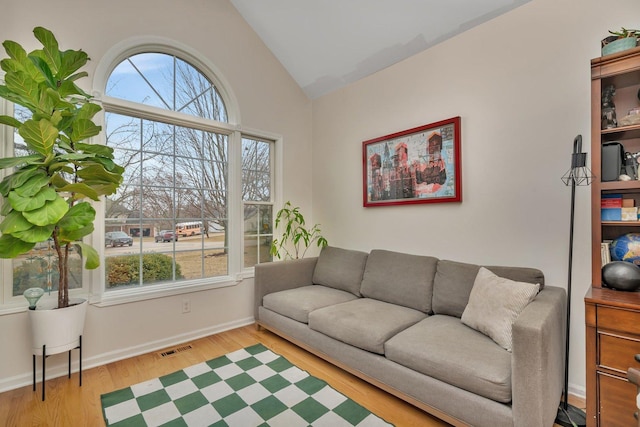 living room featuring vaulted ceiling, wood finished floors, visible vents, and a healthy amount of sunlight