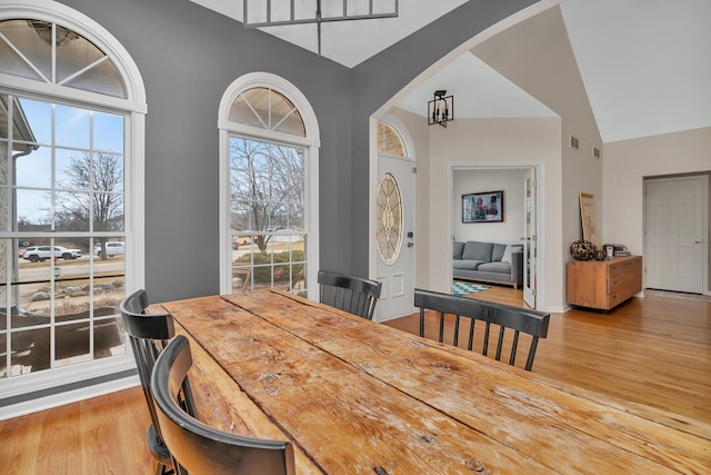 dining room featuring high vaulted ceiling, arched walkways, visible vents, and wood finished floors