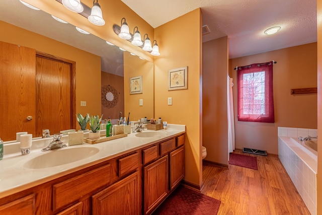 full bathroom with tiled bath, a sink, toilet, and wood finished floors