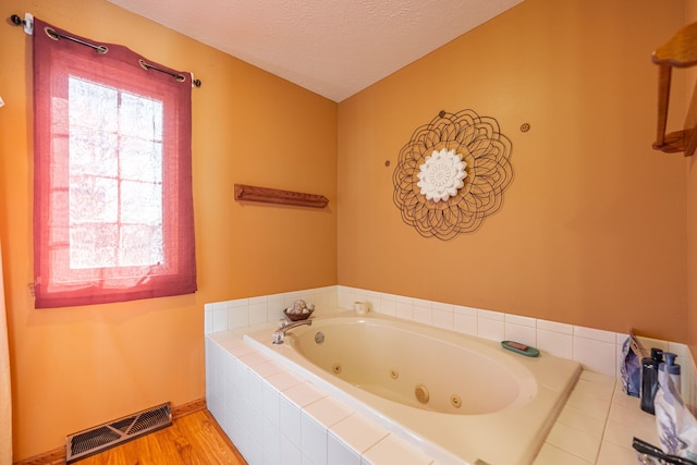 full bathroom featuring a textured ceiling, a tub with jets, wood finished floors, and visible vents