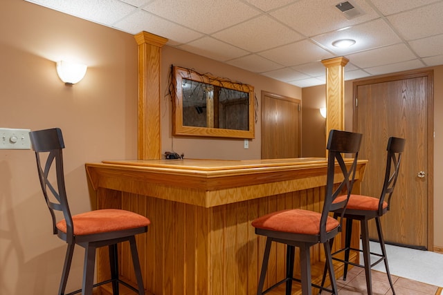 bar featuring a dry bar, ornate columns, visible vents, and a drop ceiling