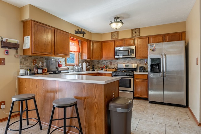 kitchen with brown cabinets, stainless steel appliances, tasteful backsplash, light countertops, and a peninsula