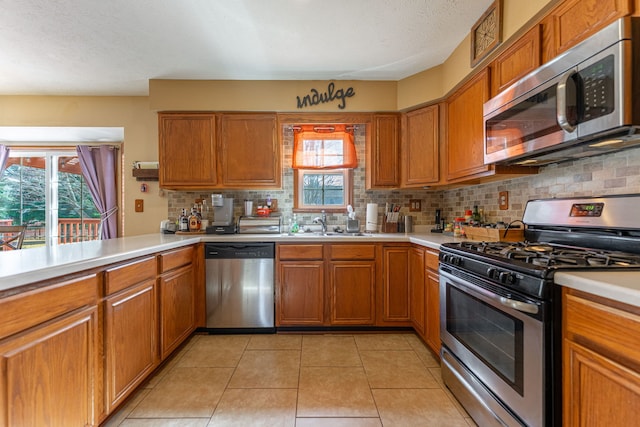 kitchen featuring brown cabinets, tasteful backsplash, light countertops, appliances with stainless steel finishes, and light tile patterned flooring