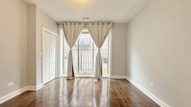 spare room with dark wood-style floors, visible vents, and baseboards