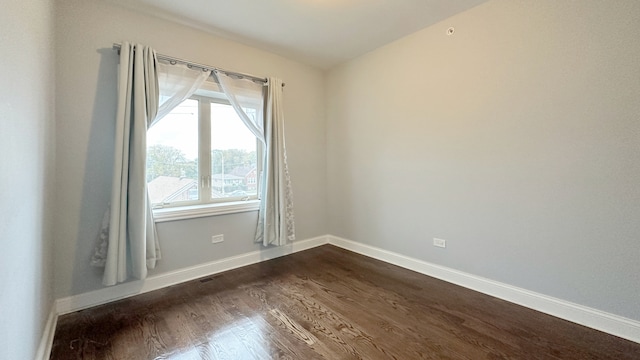 spare room with dark wood-type flooring, visible vents, and baseboards