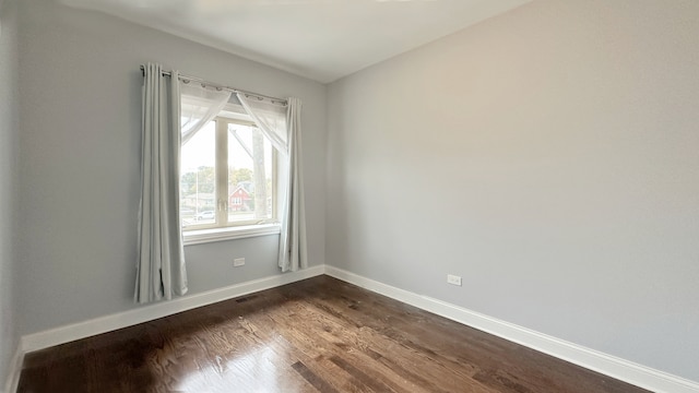 spare room with dark wood-style floors, visible vents, and baseboards