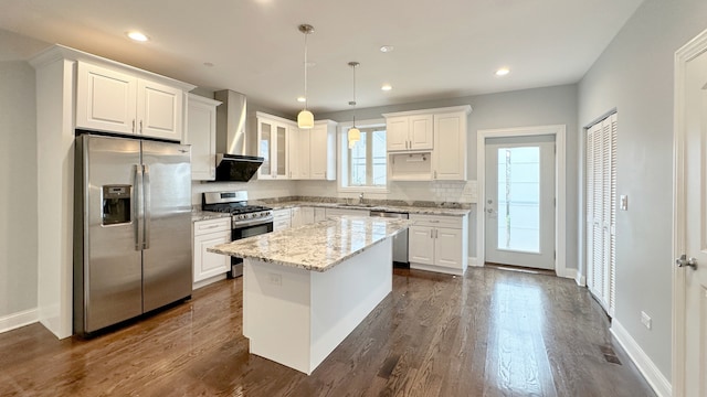 kitchen with appliances with stainless steel finishes, white cabinets, and wall chimney range hood