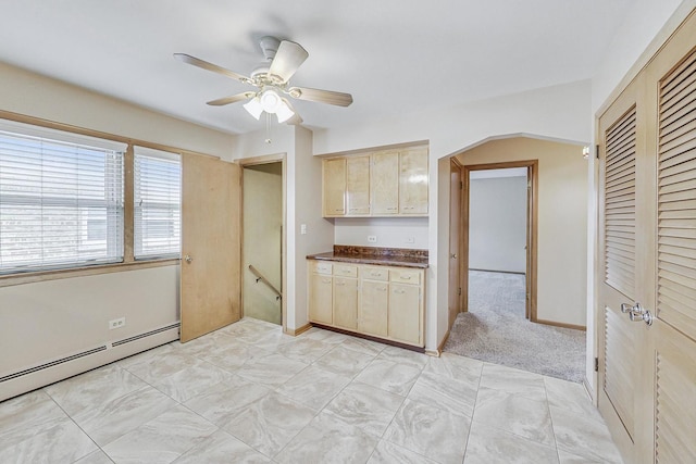 kitchen with arched walkways, a baseboard radiator, dark countertops, light brown cabinetry, and ceiling fan