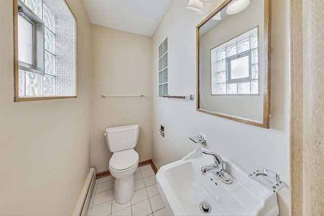 half bath with a baseboard radiator, toilet, a sink, baseboards, and tile patterned floors