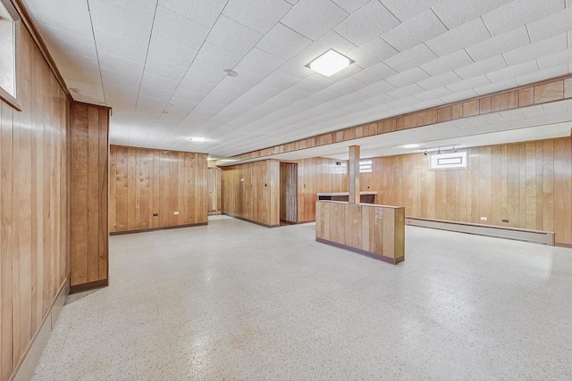 basement with a baseboard heating unit, light floors, wooden walls, and baseboards