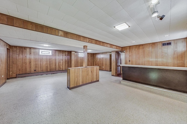 basement featuring light floors, a baseboard radiator, visible vents, and wooden walls