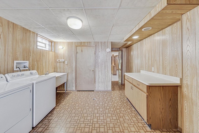 laundry room featuring cabinet space, brick patterned floor, washing machine and dryer, a sink, and wooden walls