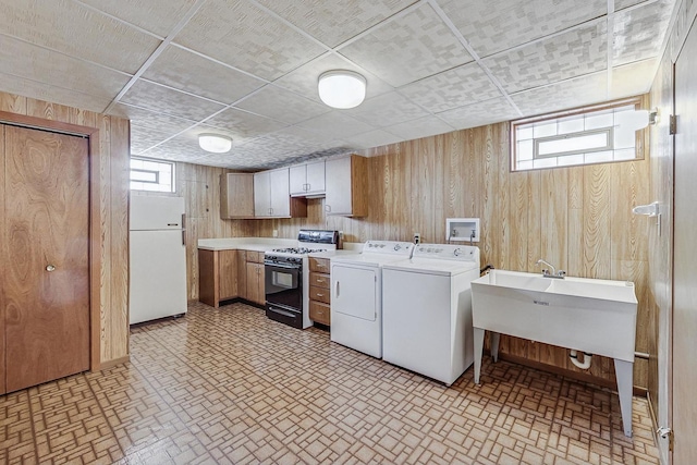 kitchen featuring washing machine and dryer, wooden walls, light countertops, freestanding refrigerator, and range with gas cooktop