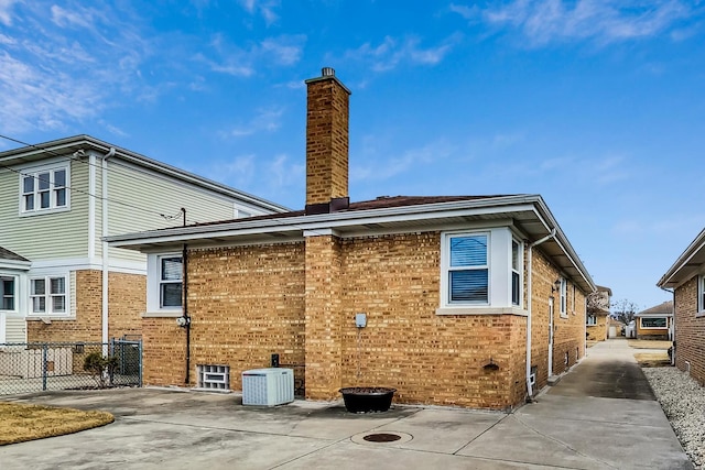 rear view of property with brick siding, a chimney, fence, and central air condition unit