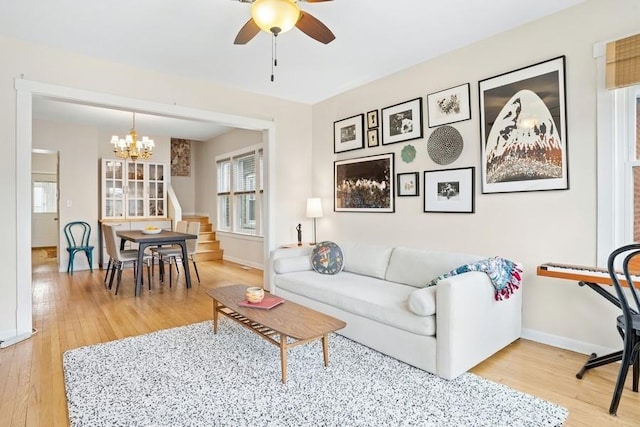 living room with light wood-type flooring, baseboards, and ceiling fan with notable chandelier