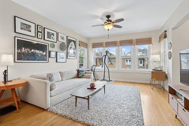 living room featuring ceiling fan, light wood finished floors, baseboards, and a healthy amount of sunlight