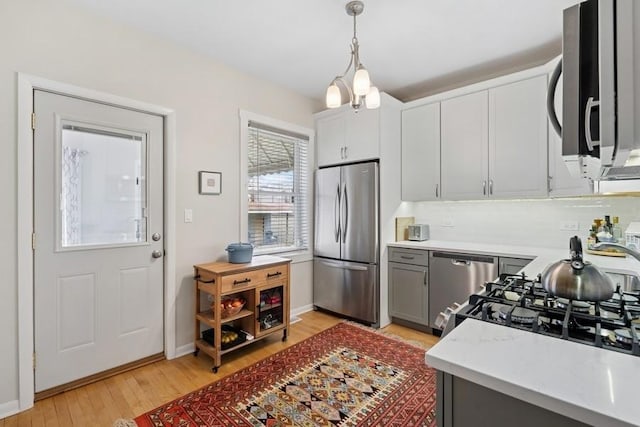 kitchen with decorative light fixtures, light countertops, light wood-type flooring, gray cabinetry, and stainless steel appliances