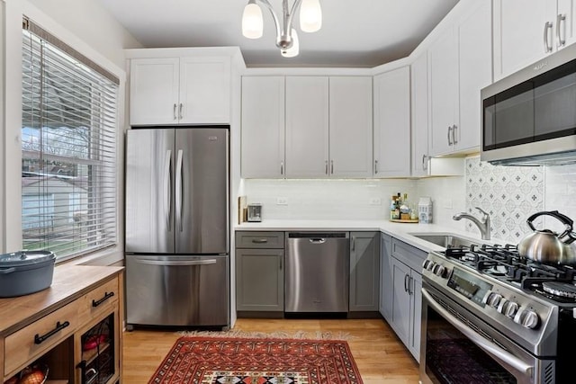 kitchen with gray cabinets, light wood-style floors, decorative backsplash, and stainless steel appliances