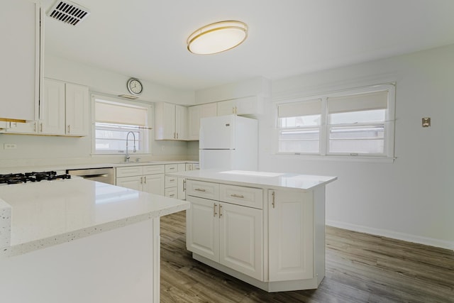 kitchen with wood finished floors, visible vents, a sink, white cabinetry, and freestanding refrigerator