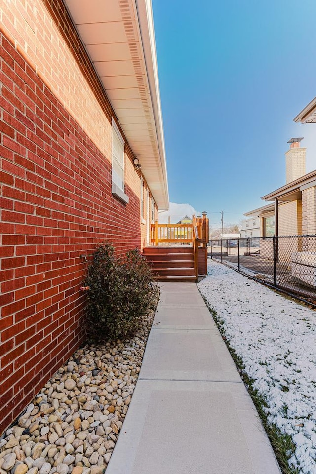 view of side of property featuring fence, a deck, and brick siding