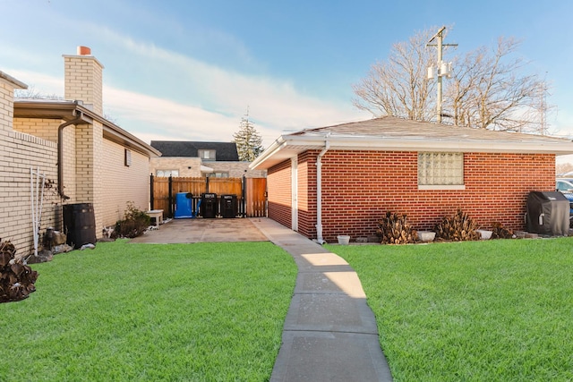 view of home's exterior with a yard, a patio area, brick siding, and fence