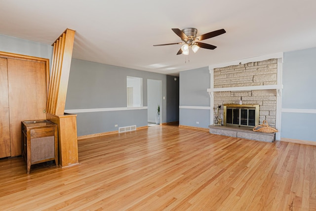 unfurnished living room featuring baseboards, visible vents, a ceiling fan, wood finished floors, and a stone fireplace