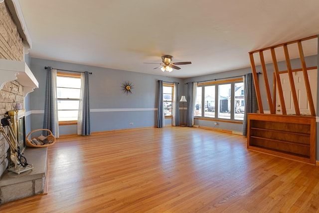 unfurnished living room featuring light wood-style floors, ceiling fan, a fireplace, and baseboards